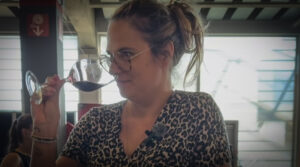 Femme humant un verre de vin rouge avec un sourire, illustrant un article sur le rapport décomplexé au vin.