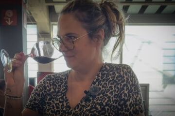 Femme humant un verre de vin rouge avec un sourire, illustrant un article sur le rapport décomplexé au vin.