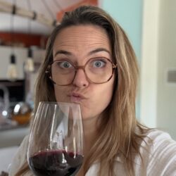 Portrait de Charlotte des itinéraires de Charlotte faisant une moue amusée en goûtant un verre de vin rouge dans une cuisine lumineuse, expression qui illustre le fait de ne pas aimer un vin sans se sentir coupable