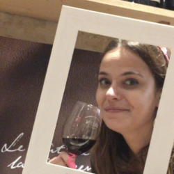 Charlotte souriante avec un verre de vin rouge à la main, moment simple et joyeux autour du vin, sans cérémonie, dans une ambiance conviviale.