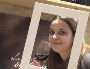 Charlotte souriante avec un verre de vin rouge à la main, moment simple et joyeux autour du vin, sans cérémonie, dans une ambiance conviviale.