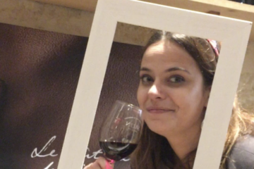 Charlotte souriante avec un verre de vin rouge à la main, moment simple et joyeux autour du vin, sans cérémonie, dans une ambiance conviviale.