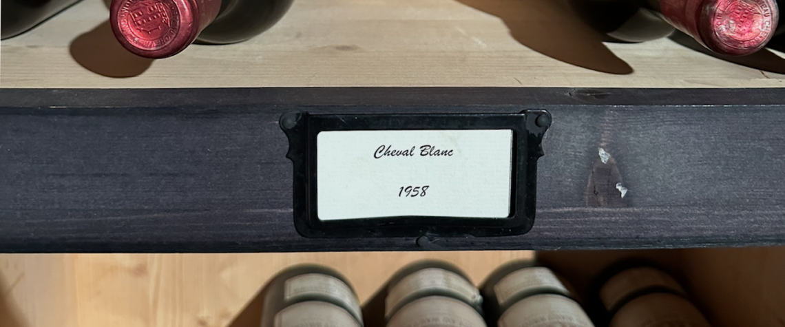 Bouteilles de vin anciennes rangées dans une cave, lumière douce sur une étagère en bois, symbole des vins qu’on garde pour des moments ou des personnes particulières.