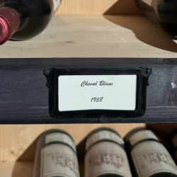 Bouteilles de vin anciennes rangées dans une cave, lumière douce sur une étagère en bois, symbole des vins qu’on garde pour des moments ou des personnes particulières.