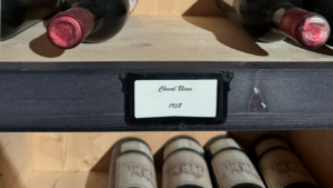 Bouteilles de vin anciennes rangées dans une cave, lumière douce sur une étagère en bois, symbole des vins qu’on garde pour des moments ou des personnes particulières.