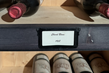 Bouteilles de vin anciennes rangées dans une cave, lumière douce sur une étagère en bois, symbole des vins qu’on garde pour des moments ou des personnes particulières.