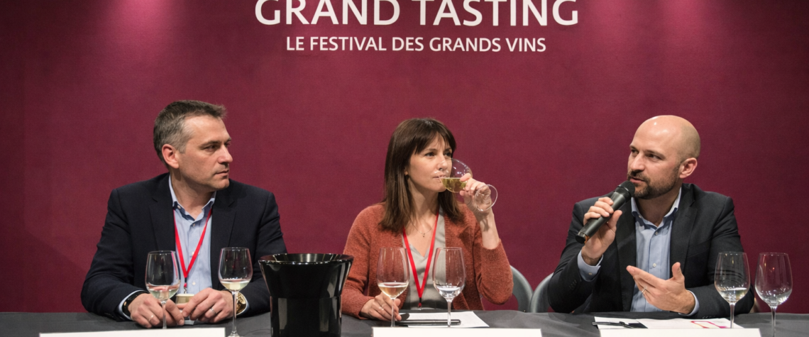 Panel de dégustation de vins lors des Primeurs de Bordeaux, trois professionnels (négociant, journaliste, courtier) assis derrière une table avec verres de dégustation et crachoir