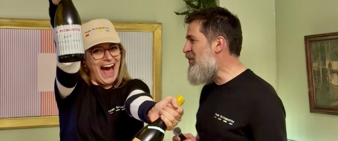 Charlotte souriante levant deux bouteilles de La Bringuette lors du lancement au Georges au Bouscat, aux côtés de Fabien le winemaker, dans une ambiance festive et conviviale.