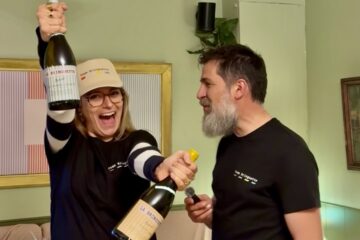 Charlotte souriante levant deux bouteilles de La Bringuette lors du lancement au Georges au Bouscat, aux côtés de Fabien le winemaker, dans une ambiance festive et conviviale.