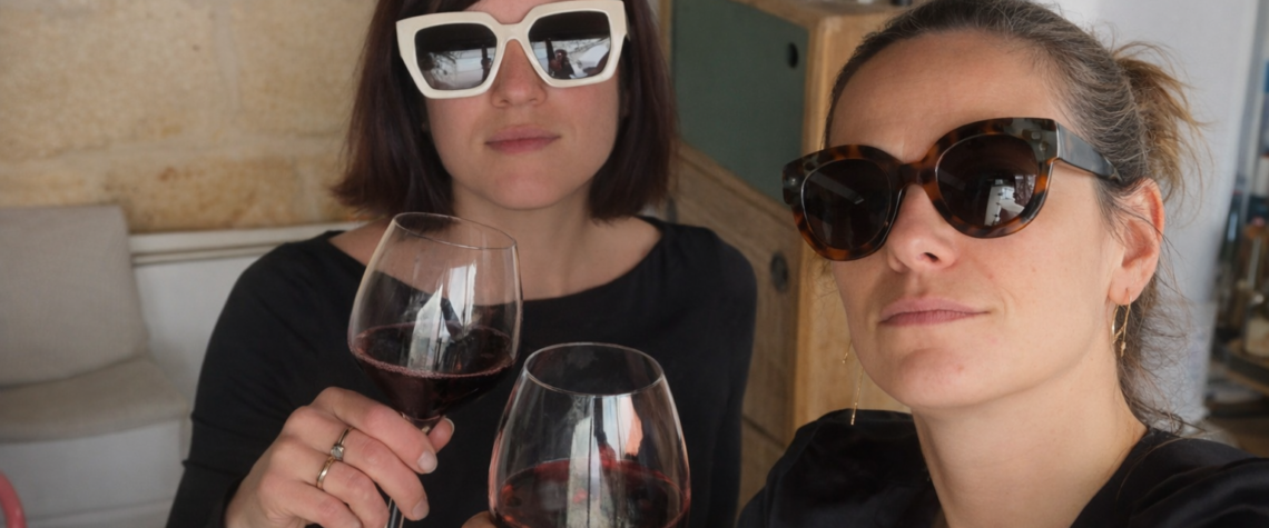 Charlotte et Marie trinquant avec des verres de vin rouge, lumière douce et ambiance chaleureuse entre amies.
