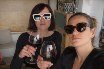 Charlotte et Marie trinquant avec des verres de vin rouge, lumière douce et ambiance chaleureuse entre amies.