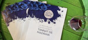 Dossier Bleu Tannat Madiran posé sur table en bois vert avec verre de vin rouge lors d’une dégustation