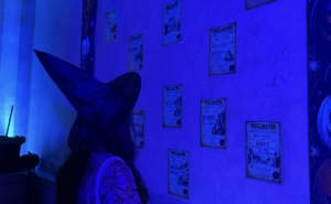 Une apprentie sorcière coiffée d'un grand chapeau pointu découvre les proclamations affichées dans une salle illuminée de bleu et violet au Château Magique de Bordeaux.