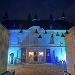 Château Siaurac illuminé de bleu pour le Château Magique de Bordeaux, avec des chapeaux de sorciers suspendus dans la cour pendant Halloween 2026.